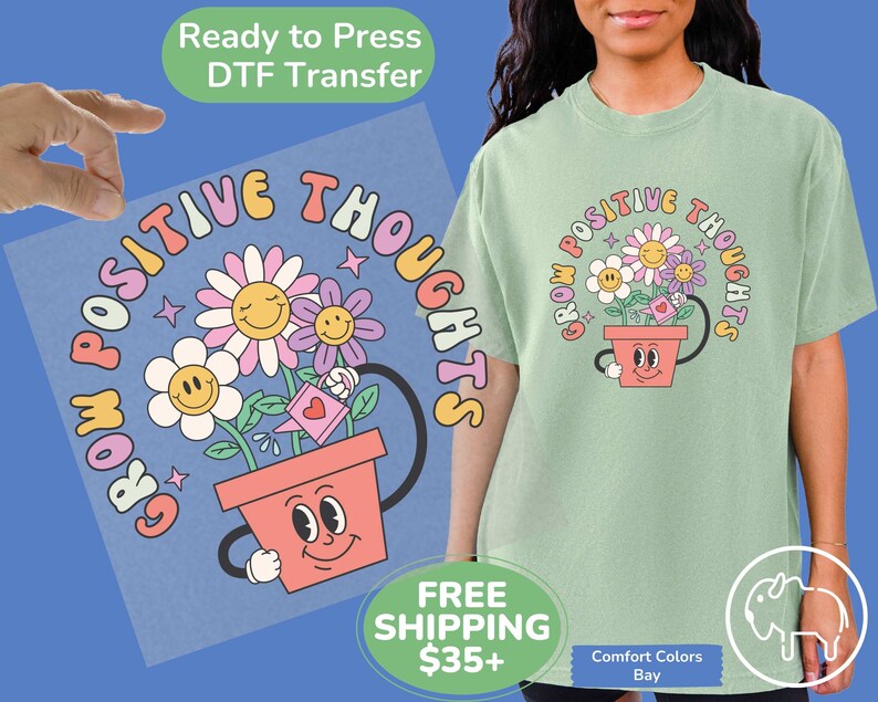 May include: A light green t-shirt with a graphic of a flower pot with smiling eyes and a watering can. The flowers in the pot have smiling faces and the text around the pot reads "Grow Positive Thoughts".