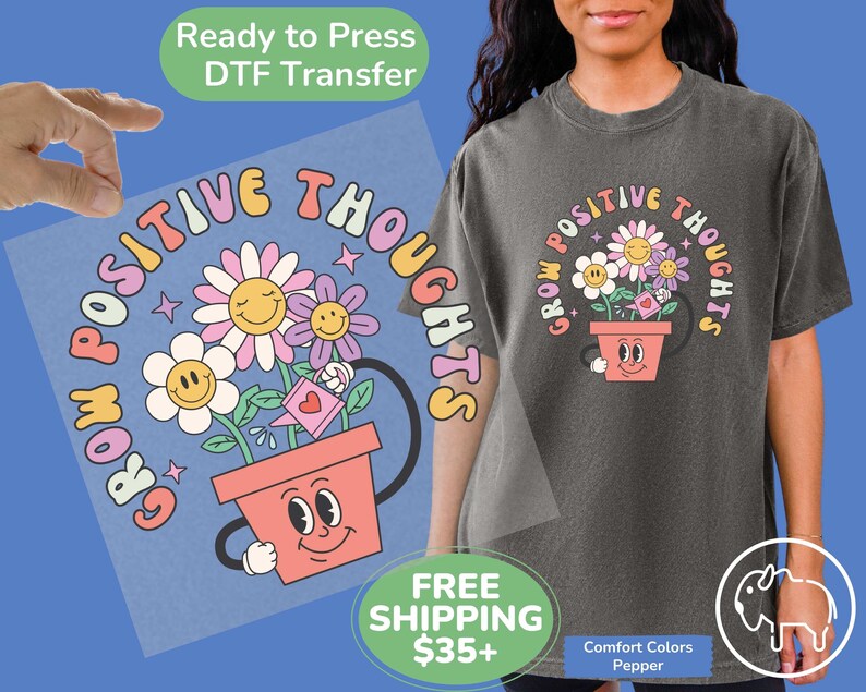 May include: A light gray t-shirt with a graphic design of a flower pot with a smiling face. The pot is filled with flowers and the text "Grow Positive Thoughts" is written in a circle around the pot.