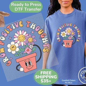 May include: A blue t-shirt with a graphic of a flower pot with a smiling face and the text "Grow Positive Thoughts".