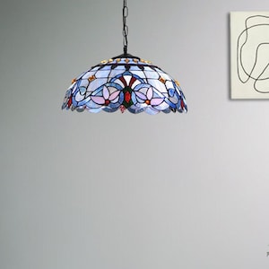 May include: A stained glass pendant light with a blue, pink, and yellow floral design. The light is hanging from a chain and is suspended from a ceiling. The light is in a room with a gray wall and a wooden floor.