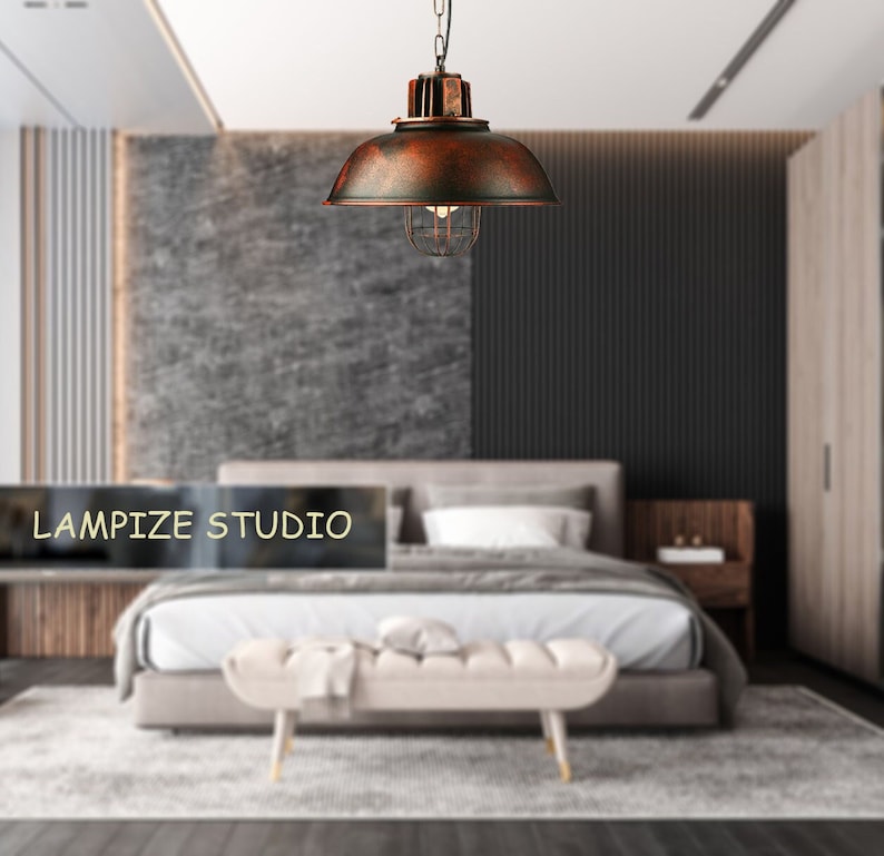 May include: A rustic, copper-colored pendant light with a cage-like shade hangs from the ceiling in a modern bedroom. The light is suspended over a bed with white bedding and a white bench at the foot of the bed. The text "LAMPIZE STUDIO" is visible in the lower left corner of the image.