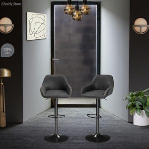 Puede incluir: Dos taburetes de bar giratorios tapizados en gris con bases y reposapi&eacute;s de metal negro. Los taburetes est&aacute;n en una habitaci&oacute;n con una puerta, una l&aacute;mpara y una pared con una pintura abstracta en blanco y negro.