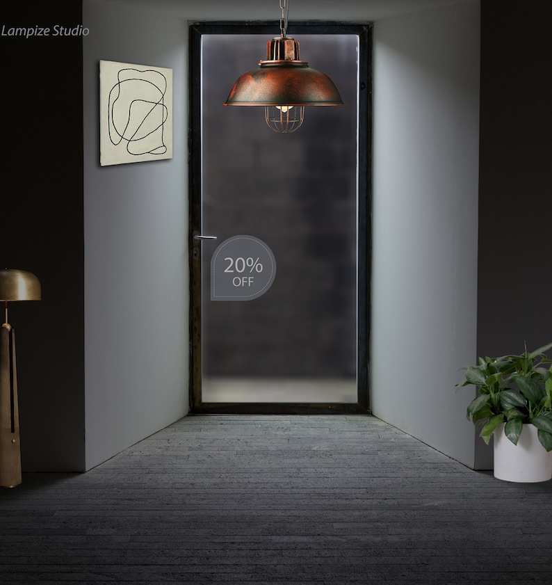 May include: A rusty brown metal pendant light with a cage-like shade hangs from the ceiling in a room with a gray wall and a door. The door has a frosted glass panel with a white sticker that says "20% OFF".