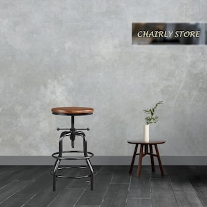 May include: A black metal swivel bar stool with a round wooden seat. The stool has a footrest and a metal base. The stool is in front of a grey wall with a sign that says "Chairly Store".