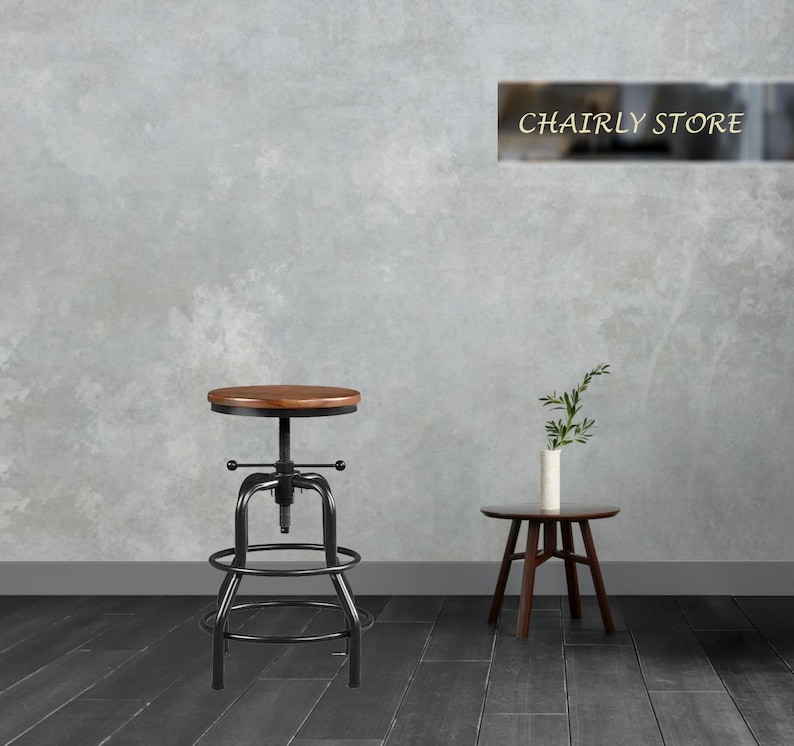 May include: A black metal swivel bar stool with a round wooden seat. The stool has a footrest and a metal base. The stool is in front of a grey wall with a sign that says "Chairly Store".