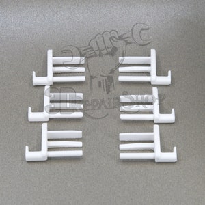 Puede incluir: Seis clips de plástico blanco con tres puntas y un gancho en un extremo. Los clips están dispuestos en dos filas de tres.