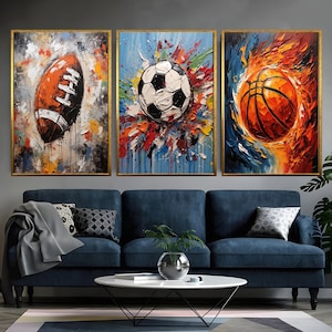 May include: Three framed abstract paintings of sports balls. The first painting features a brown and white football with colourful paint splatters. The second painting features a black and white football with colourful paint splatters. The third painting features an orange and brown basketball with orange and yellow paint splatters.
