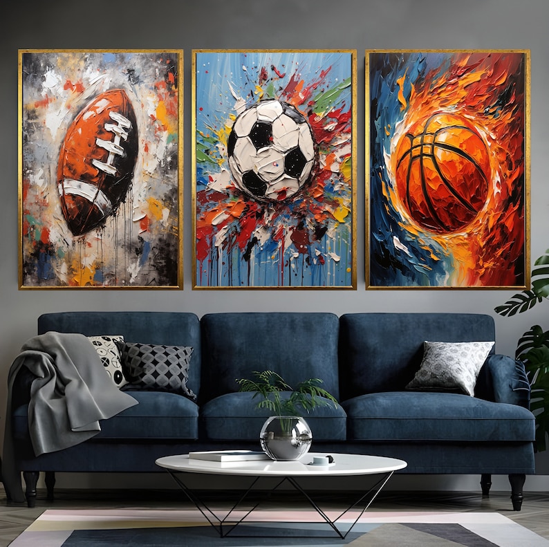 May include: Three framed abstract paintings of sports balls. The first painting features a brown and white football with colourful paint splatters. The second painting features a black and white football with colourful paint splatters. The third painting features an orange and brown basketball with orange and yellow paint splatters.