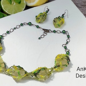 May include: A green and yellow beaded necklace with a geometric design and matching earrings. The necklace features a series of large, faceted beads that are connected by a delicate chain. The earrings are similar in design to the necklace, with smaller versions of the faceted beads. The jewelry is set against a white background. AnKor Design.
