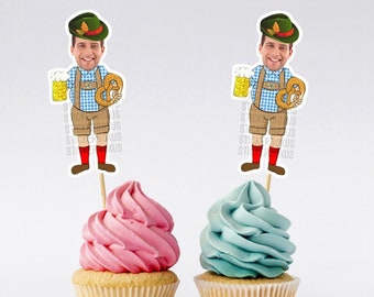 May include: Two cupcakes with pink and blue frosting topped with a  toothpick holding a printed image of a man wearing a traditional German hat, holding a beer stein and a pretzel.
