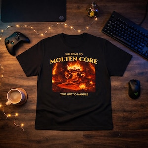 Könnte beinhalten: Schwarzes T-Shirt mit dem Text "WELCOME TO MOLTEN CORE" über einer feurigen Grafik und "TOO HOT TO HANDLE" darunter. Das Bild befindet sich auf einer Holzoberfläche mit Tastatur, Maus und Gamecontroller.