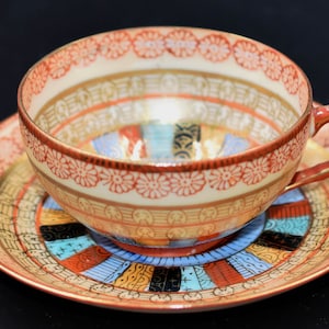 Könnte beinhalten: Ein Vintage-Teetassen- und Untertassen-Set mit einem roten, weißen und goldenen Blumenmuster. Die Untertasse hat ein farbenfrohes geometrisches Design.