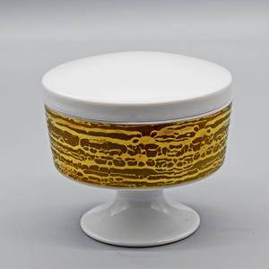 May include: White ceramic sugar bowl with a gold patterned design. The bowl has a lid and sits on a pedestal base.