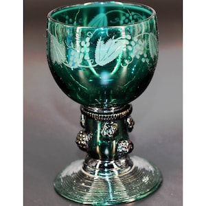 May include: A green glass goblet with a vine design etched into the side. The goblet has a silver-colored base with decorative knobs.