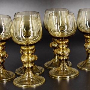 May include: Set of six amber glass wine glasses with a unique, textured stem and base. The glasses have a round bowl and a wide, flared foot.