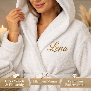 Könnte beinhalten: Ein weißer Bademantel mit Kapuze und dem Namen "Lena" in goldener Schrift gestickt. Der Plüsch-Bademantel hat einen Schalkragen und einen Bindegürtel. Das Bild enthält auch den Text "Ultra Weich & Flauschig", "Mit Ihrem Namen" und "Premium Bademantel".