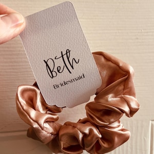 May include: A peach-coloured satin scrunchie with a white tag that says "Beth Bridesmaid".