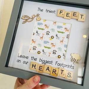 Op de afbeelding: Een grijs fotolijstje met een witte passe-partout en een foto erin. De foto heeft een jungledierenprint achtergrond. Het lijstje heeft houten lettertegels die "The tiniest feet leave the biggest footprints on our hearts" spellen.