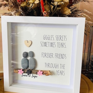 Könnte beinhalten: Weiß gerahmtes Kunstwerk mit dem Text "Giggles, Secrets, Sometimes Tears. Forever Friends Through The Years." Enthält Kieselkunst von zwei Figuren, ein Holzherz und rosa Blumen. Enthält die Namen "Janine & Jayne".