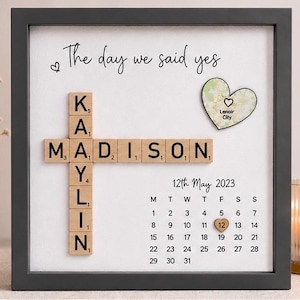 May include: Framed artwork with the text "The day we said yes." The names Kaylin Madison are spelled out with wooden Scrabble tiles. A heart-shaped map of Lenoir City is included, along with a calendar highlighting May 12, 2023.
