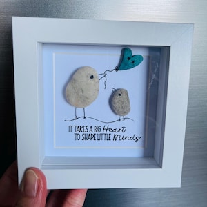 以下が含まれることがあります： 2羽の石の鳥が描かれた額縁付きの芸術作品。1羽は青いハート型の風船を持っています。テキストには「小さな心を形作るには大きな心が必要だ」と書いてあります。