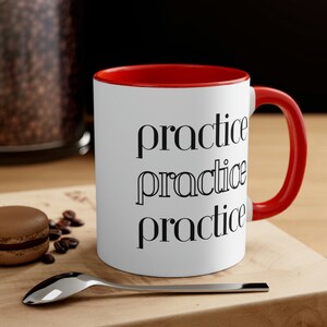 Pode incluir: Caneca de cerâmica branca com borda e alça vermelhas. A caneca tem as palavras "practice practice practice" impressas em preto na frente.