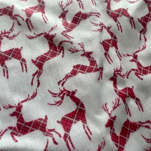 Op de afbeelding: Witte stof met een herhalend patroon van rode geruite rendieren. De rendieren kijken in verschillende richtingen en hebben geweien.