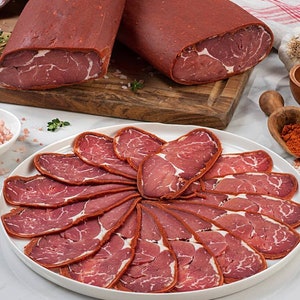 May include: A white plate with thinly sliced, dried, red meat arranged in a circular pattern. The meat is a traditional Turkish delicacy called pastırma.