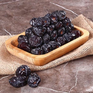 May include: A wooden bowl filled with a large pile of dark, dried dates. The dates are arranged in a pyramid shape and are surrounded by a burlap cloth.