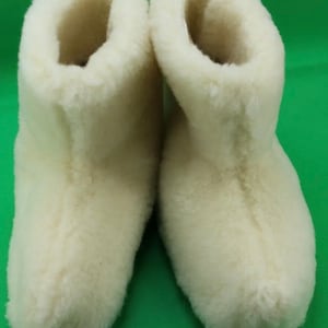 Puede incluir: Un par de zapatillas de piel de oveja blancas. Las zapatillas están hechas de piel de oveja suave y esponjosa y tienen la punta cerrada.