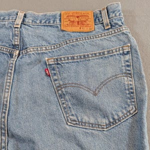 Puede incluir: Primer plano de unos vaqueros de mezclilla azul claro. La parte trasera de los vaqueros presenta un bolsillo, una etiqueta roja de Levi Strauss & Co. y un parche de cuero marrón con el logotipo de Levi Strauss & Co. y la información de la talla. La cintura es de 107 cm y la entrepierna es de 76 cm.