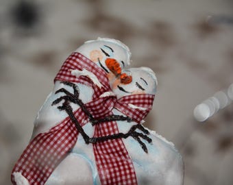 May include: Two snowman figures embracing, each with a red and white checkered scarf. The snowmen have black stick arms, orange carrot noses, and closed eyes. The snowmen are white with light blue shading.