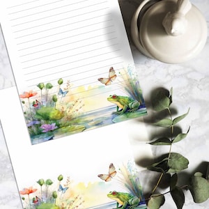 Może przedstawiać: Dwie akwarelowe ilustracje zielonej żaby siedzącej na liściu lilii wodnej w stawie. Żaba ma czerwone oczy i jest otoczona zielonymi liśćmi lilii wodnej, wodą i kolorowymi kwiatami. Motyle latają nad stawem.