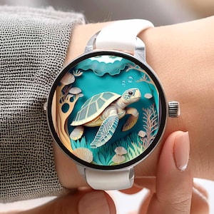 Pode incluir: Um smartwatch redondo com uma pulseira branca e uma caixa prateada. O mostrador exibe uma ilustração detalhada de uma tartaruga marinha nadando em uma cena subaquática com água turquesa, plantas e bolhas. O relógio está sendo usado em um pulso.