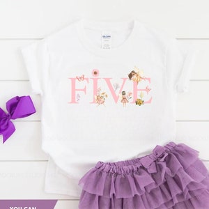 May include: A white short-sleeved t-shirt with the word FIVE printed in pink, featuring fairy and floral illustrations within the letters, paired with a purple layered tulle skirt and a matching purple hair bow. Text reads: YOU CAN CUSTOMIZE IT TO ANY AGE!