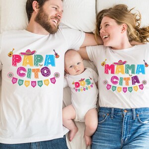 Peut inclure: Une famille de trois personnes portant des t-shirts blancs assortis avec du texte et des motifs color&eacute;s. Les t-shirts disent "Papa Cito", "Mama Cita" et "Dos".