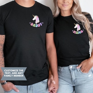 Puede incluir: Camisetas negras con un dise&ntilde;o de unicornio. Una camiseta dice "Daddy" y la otra "Mama" en texto colorido. Las camisetas son de manga corta y tienen cuello redondo.