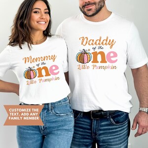 Puede incluir: Dos camisetas blancas con un dise&ntilde;o de calabaza y texto que dice "Mommy of the One Little Pumpkin" y "Daddy of the One Little Pumpkin".