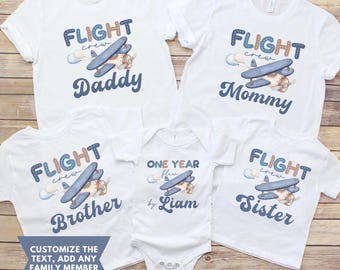 May include: A set of five white t-shirts with a blue and brown airplane graphic and the text "FLIGHT crew" on each shirt. The shirts are personalized with the text "Daddy", "Mommy", "Brother", "Sister", and "One Year Flew by Liam".