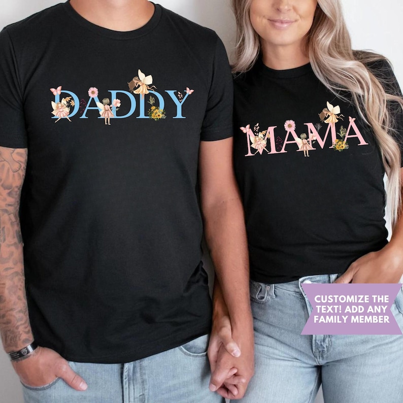 May include: Two black t-shirts featuring graphic designs. The left shirt displays the word DADDY in light blue with fairy and floral accents. The right shirt displays the word MAMA in light pink with similar fairy and floral accents.