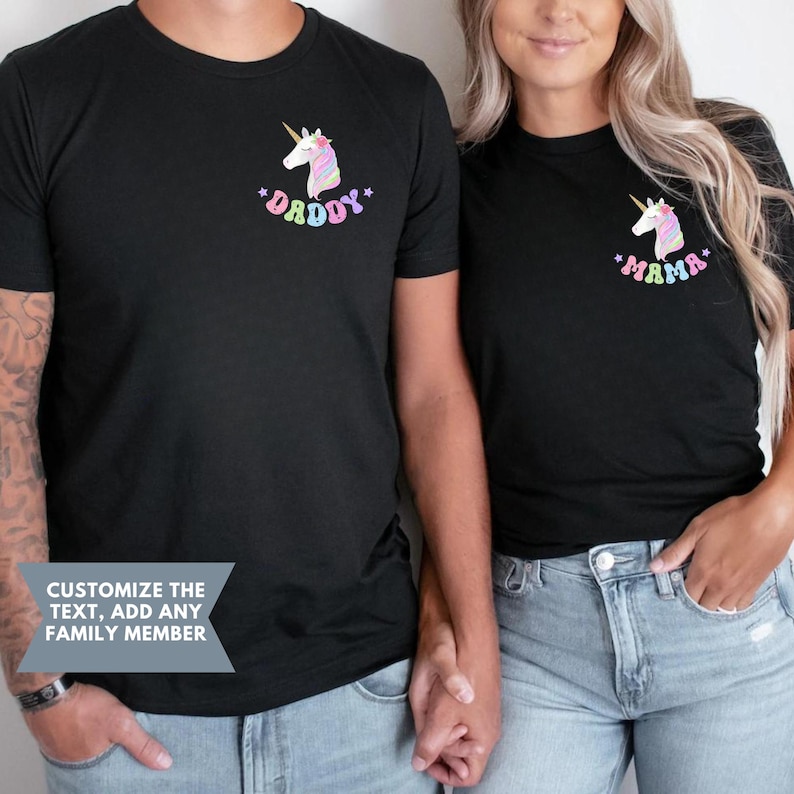 Puede incluir: Camisetas negras con un dise&ntilde;o de unicornio. Una camiseta dice "Daddy" y la otra "Mama" en texto colorido. Las camisetas son de manga corta y tienen cuello redondo.