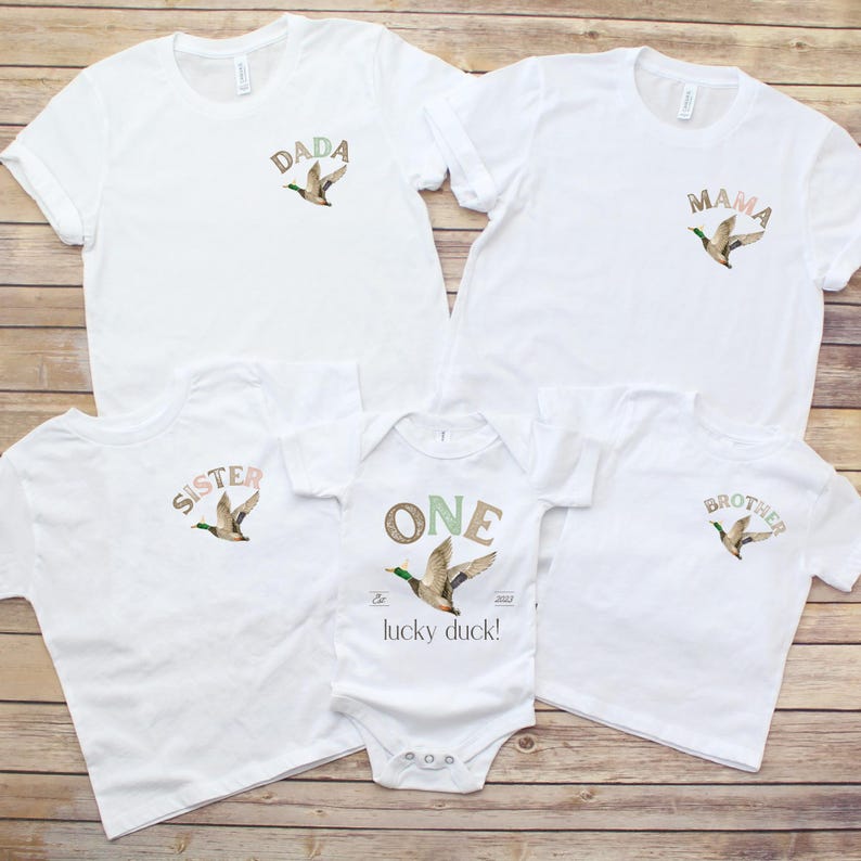 May include: A set of five white t-shirts with a duck and text on each. The shirts say "Dada", "Mama", "Sister", "Brother", and "One - The Lucky Duck! 2023".