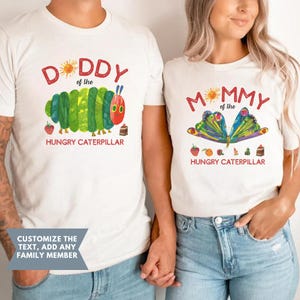 Może przedstawiać: Dwie pasujące białe koszulki z ilustracjami z "Bardzo głodnej gąsienicy". Jedna z napisem "DADDY" i gąsienicą, druga z "MOMMY" i motylem. Pod każdym obrazkiem napis "HUNGRY CATERPILLAR".