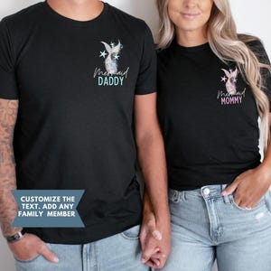 May include: Black t-shirts with mermaid tail and star graphics. One shirt says "Mermaid Daddy" in blue, the other says "Mermaid Mommy" in pink. The shirts are worn by a couple holding hands. Text on the bottom says "Customize the text. Add any family member."