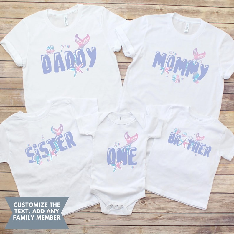 May include: Set of five white t-shirts with a mermaid tail and sea-themed designs. The shirts say "Daddy", "Mommy", "Sister", "One", and "Brother".
