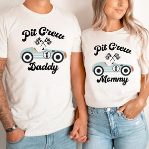 May include: Two white t-shirts with a blue race car graphic and the text "Pit Crew Daddy" and "Pit Crew Mommy".