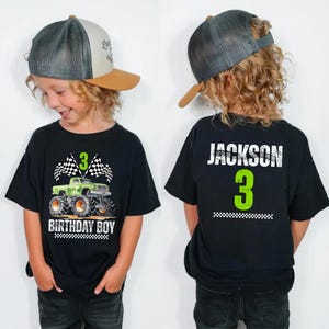 Puede incluir: Camiseta negra con un dise&ntilde;o de cami&oacute;n monstruo verde y el texto "3 BIRTHDAY BOY". La parte trasera de la camiseta tiene el nombre "JACKSON" y el n&uacute;mero "3". La camiseta la lleva un ni&ntilde;o.