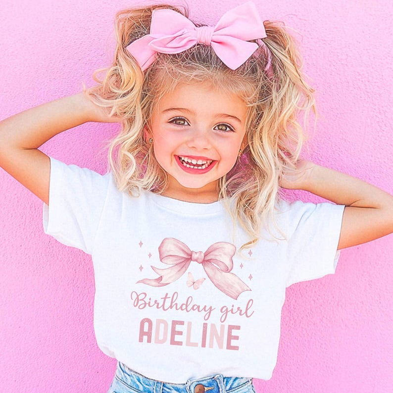Puede incluir: Camiseta blanca con un lazo rosa y el texto "Birthday girl ADELINE" impreso en ella. Una ni&ntilde;a lleva la camiseta y tiene un lazo rosa en el pelo.