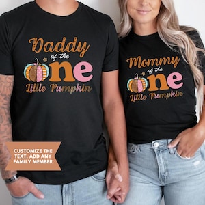 Puede incluir: Dos camisetas negras con un dise&ntilde;o de calabaza y el texto "Daddy of the one Little Pumpkin" y "Mommy of the one Little Pumpkin".