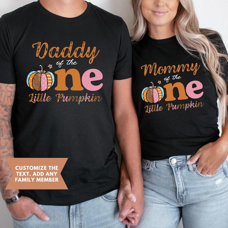 Puede incluir: Dos camisetas negras con un dise&ntilde;o de calabaza y el texto "Daddy of the one Little Pumpkin" y "Mommy of the one Little Pumpkin".